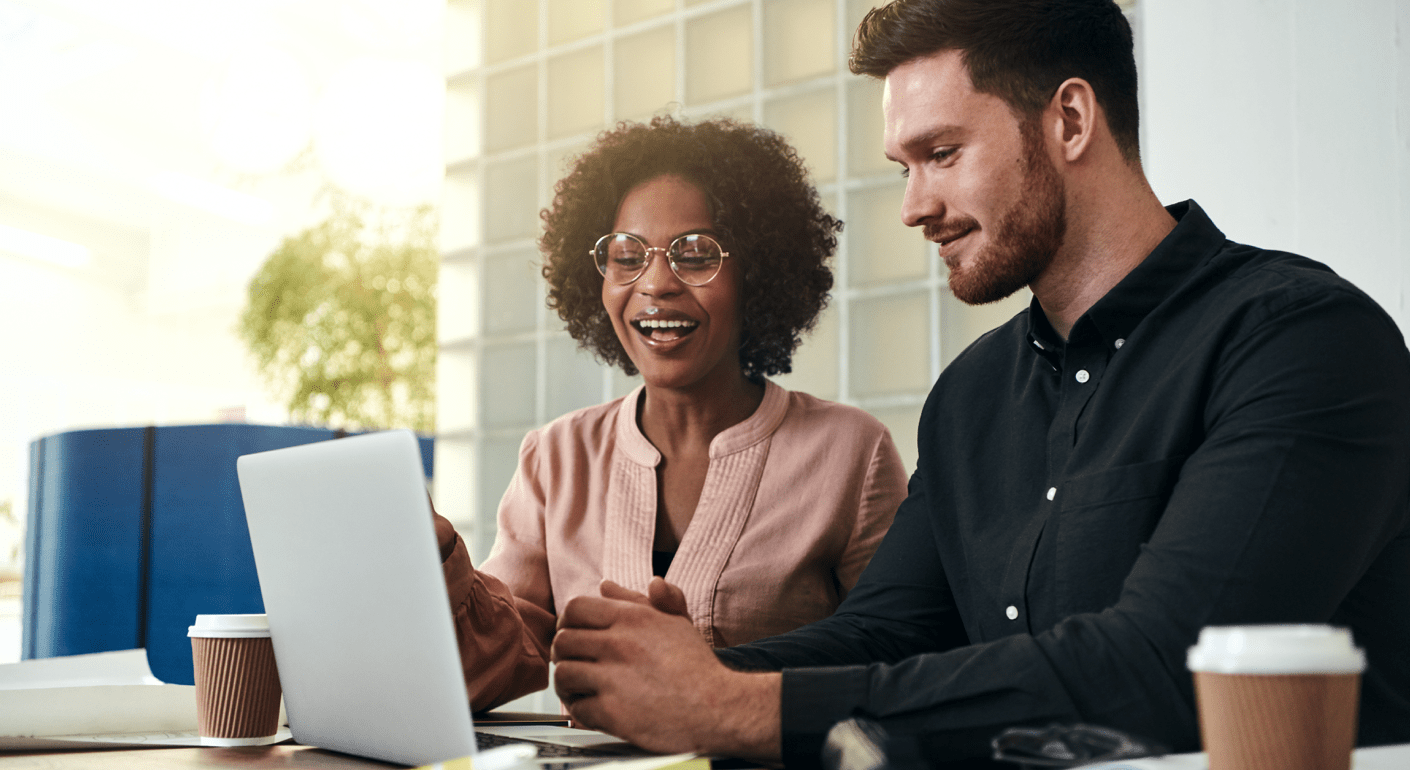 Smiling woman points to laptop computer screen to man who sits beside her. 